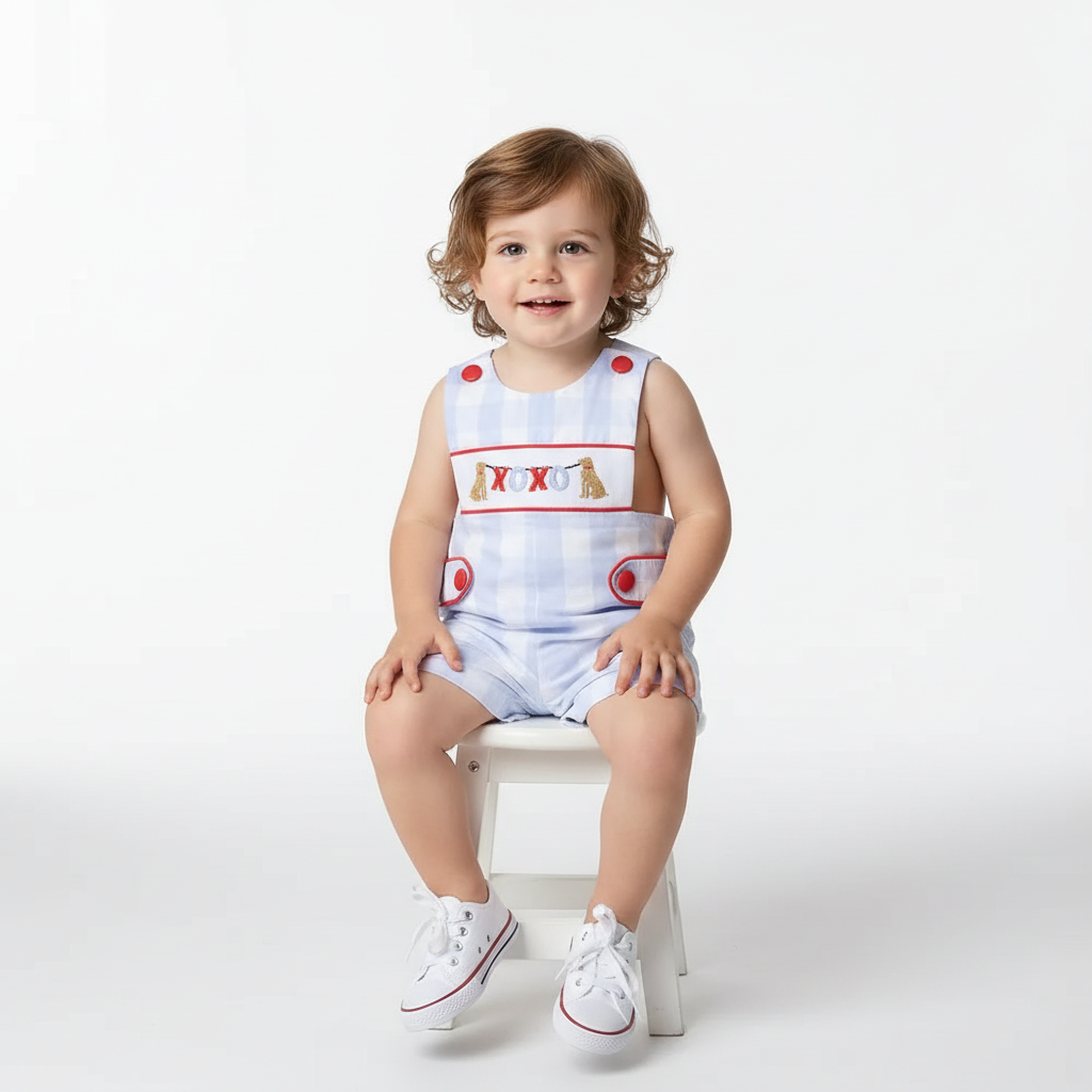 toddler boy wearing SMOCKED BOYS XOXO DOG shortall with blue check pattern and red buttons sitting on white stool