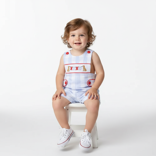 toddler boy wearing SMOCKED BOYS XOXO DOG shortall with blue check pattern and red buttons sitting on white stool