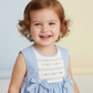 Toddler wearing a blue sundress with smocked panel and bows, smiling.