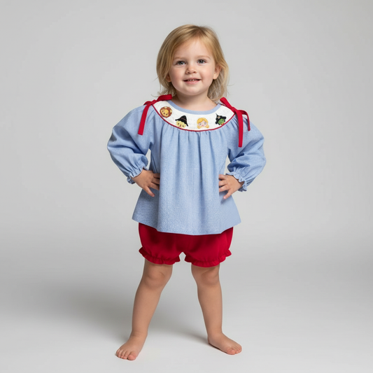 Toddler girl wearing smocked OZ bloomer set with red bows and character neckline.